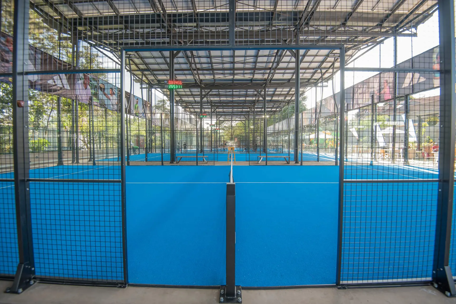 Two padel courts seen end-on under the continuous roof.