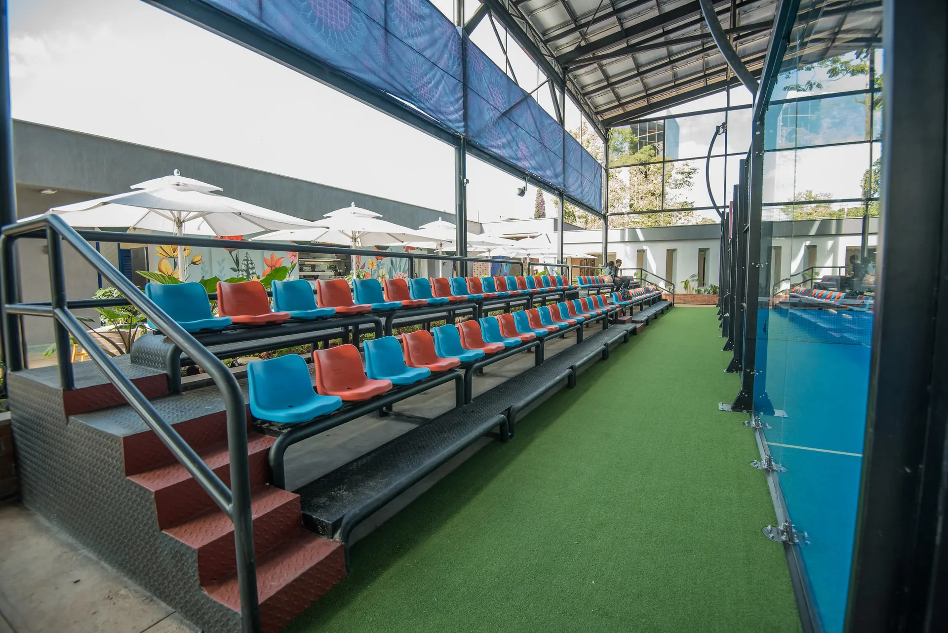 Tiered spectator seating in bright blue and red beside the courts.